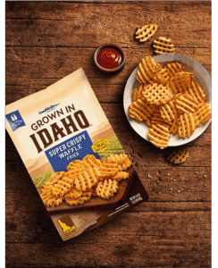 Plate of waffle cut fries on wooden table.